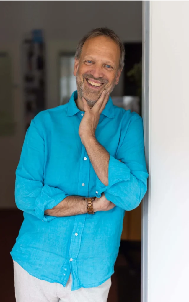 Andreas Deutsch in türkisen Hemd, Paartherapeut und Familienberater, lacht und steht entspannt im Türrahmen
