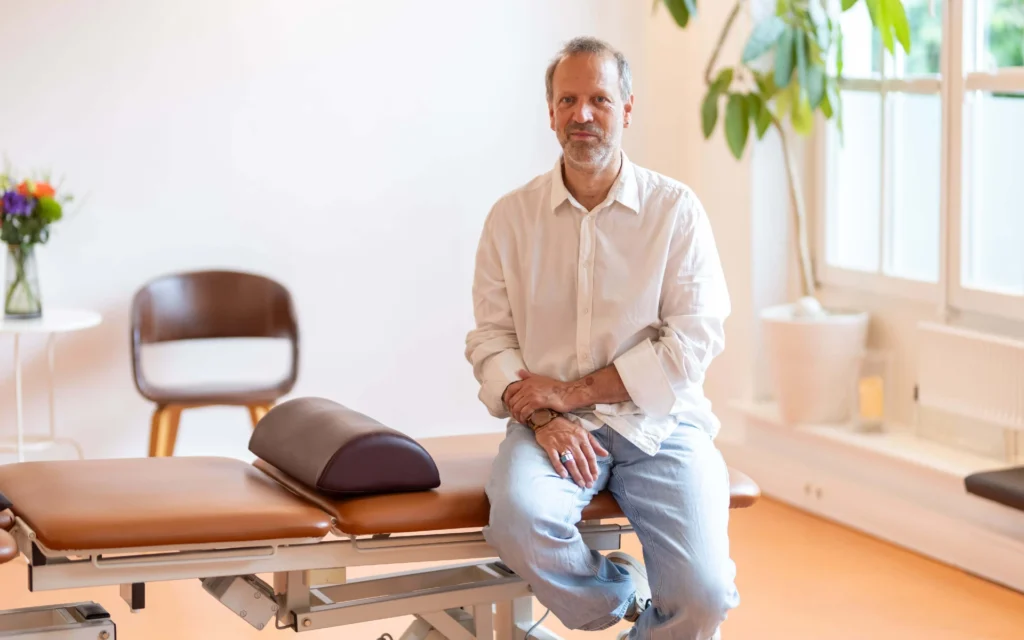 Andreas Deutsch, Physiotherapeut in Hamburg, sitzt entspannt auf einer Behandlungsliege in seiner Praxis