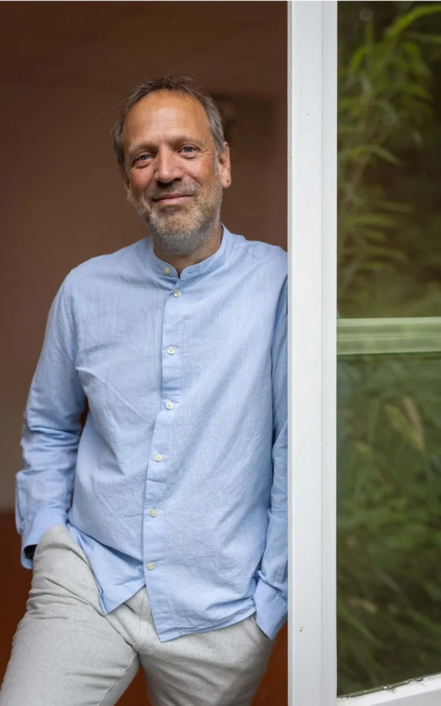 Systemischer Coach Andreas Deutsch aus Hamburg lehnt entspannt am Fensterrahmen und blickt freundlich in die Kamera